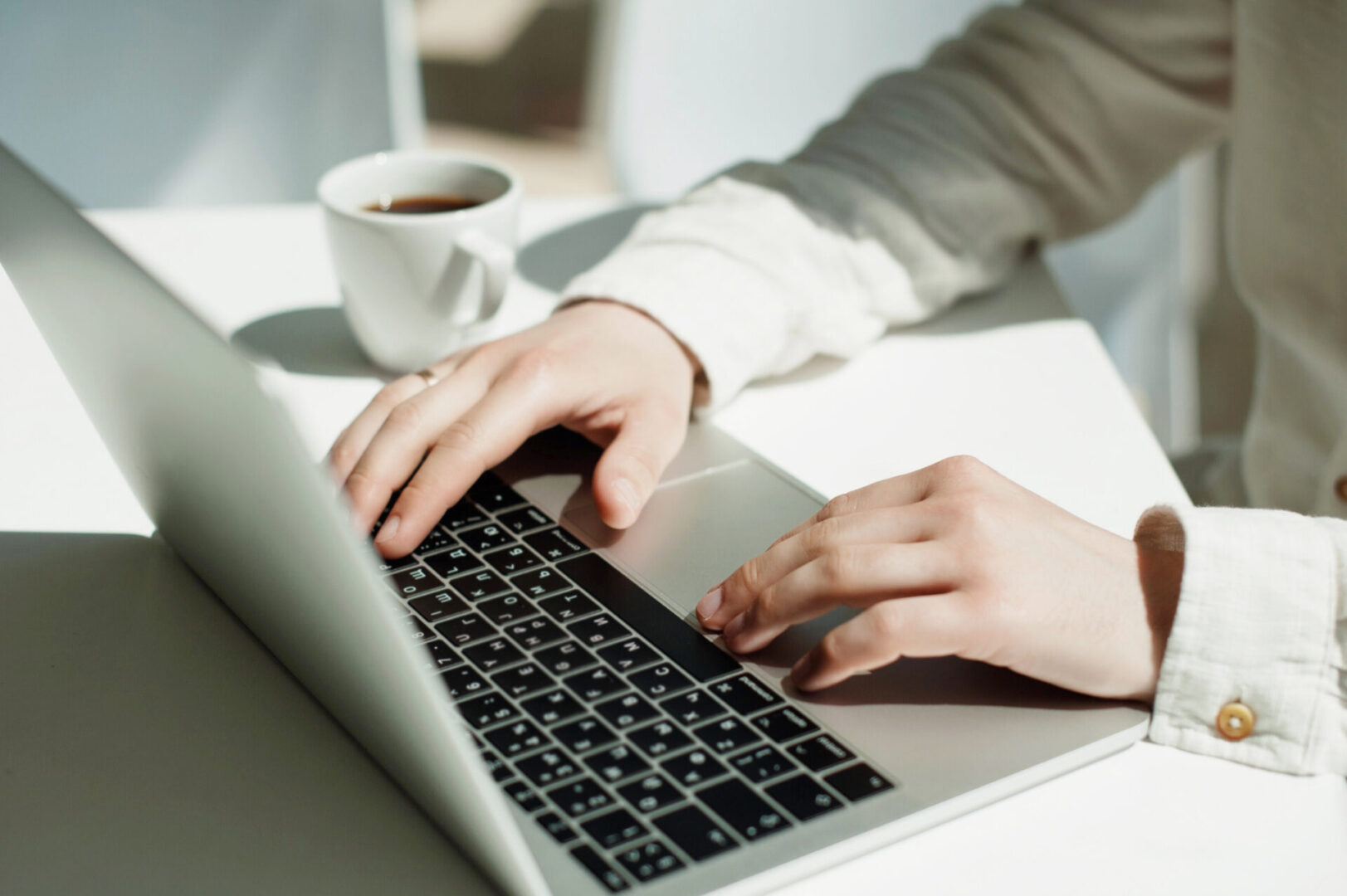 Hands typing on laptop with coffee cup